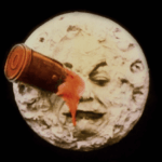 A still frame from the silent film "A Trip to the Moon" showing a rocket capsule embedded in the right eye of the man in the moon, who blinks and sticks out his tongue as blood drips from the impact site.