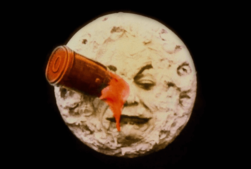A still frame from the silent film "A Trip to the Moon" showing a rocket capsule embedded in the right eye of the man in the moon, who blinks and sticks out his tongue as blood drips from the impact site.